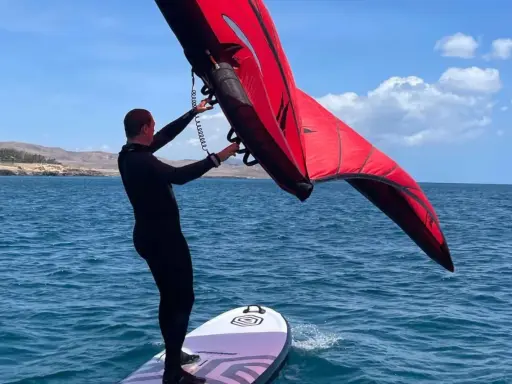 Mann mit rotem Wingboard auf dem Wasser vor Costa Calma. Perfekter Tag für Wassersport am Ion Club.