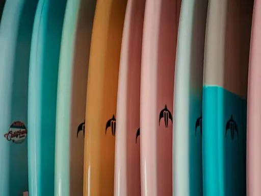 Reihe bunter Surfboards in Pastelltönen. Welches Surfboard passt zu mir? Die Auswahl ist groß, von hellblau bis rosa.