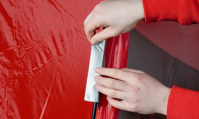 Hände flicken ein rotes Zelt mit silbernem Klebeband.