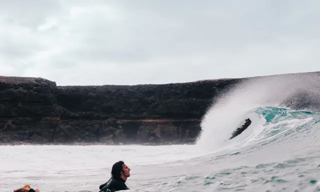 Surfer wartet auf die perfekte Welle vor der Felsküste. Windsurfen Fuerteventura.