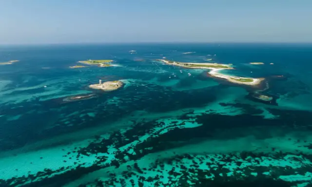 Türkisblaues Wasser umgibt die Glenan Inseln mit einem Leuchtturm auf einer kleinen Insel.
