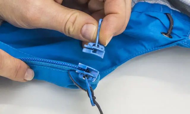 Hände tauschen den blauen Reißverschluss-Zipper an einer Jacke aus.