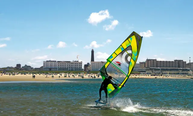 Windsurfer auf dem Meer vor Borkum, im Hintergrund der Strand mit Menschen und Hotels.