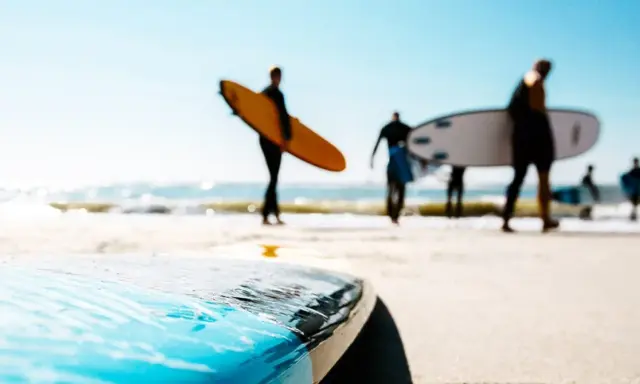 Surfer in Holland tragen ihre Boards zum Wasser. Die Sonne scheint, die Wellen brechen.