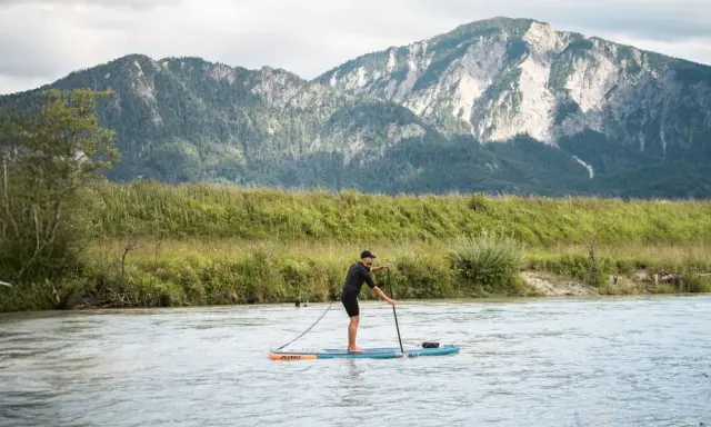 Mann auf SUP-Board, der geradeaus fährt, mit Bergen im Hintergrund.