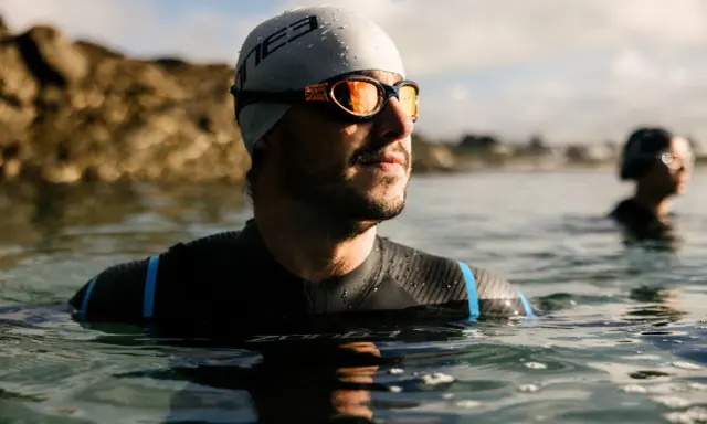 Mann mit Schwimmbrille und Badekappe im Wasser, bereit für das Schwimmen. Die Schwimmbrille reinigen ist wichtig für klare Sicht.