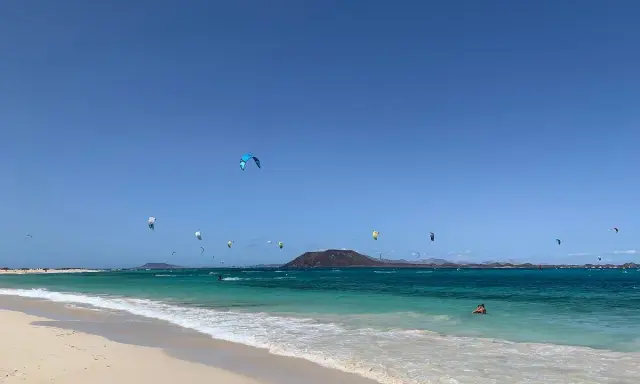 Kitesurfer tanzen über das türkisfarbene Wasser am Flag Beach Corralejo. Ein einsamer Schwimmer genießt die Sonne.