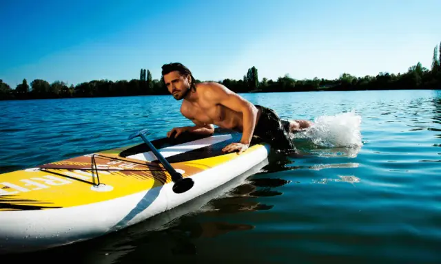Mann liegt auf SUP-Board, paddelt mit Armen im Wasser. Perfekt für eine SUP Tour auf dem See.