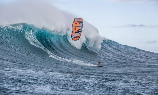 Ein Kitesurfer reitet eine riesige Welle bei Jaws, Hawaii. Die Welle bricht mit gewaltiger Kraft, während der Surfer mit seinem Kite in der Luft schwebt.