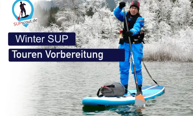 Person im blauen Neoprenanzug bereitet sich auf eine Winter SUP Tour vor. Die Landschaft ist mit Schnee bedeckt.