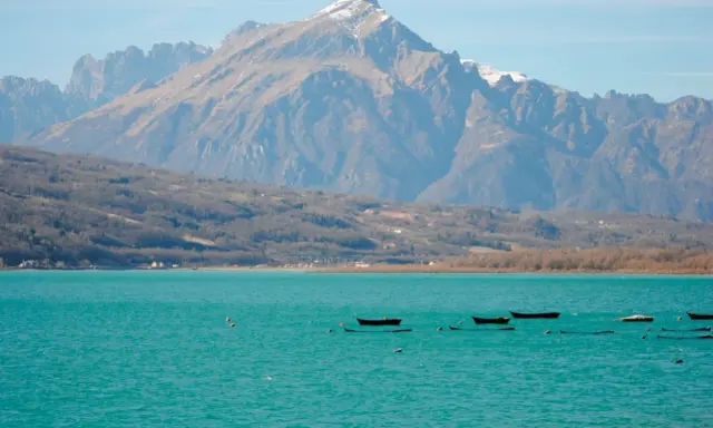 Boote treiben auf dem türkisfarbenen Lago di Santa Croce vor einer majestätischen Bergkulisse.