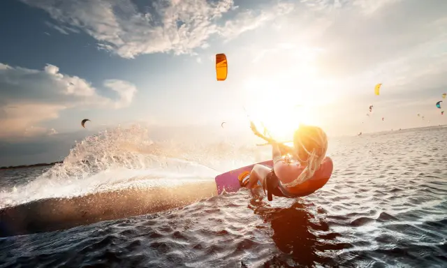 Kitesurferin genießt das Rhodos Surfen im goldenen Abendlicht, spritzt Wasser auf.