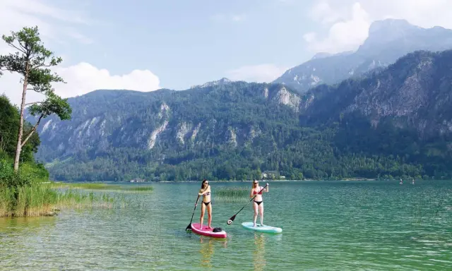 Zwei Frauen genießen Stand-Up-Paddling auf einem ruhigen See vor einer Bergkulisse. Perfekte sup spots für einen entspannten Tag.