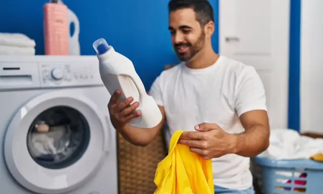 Mann hält Waschmittel und gelbes Trikot bereit, um die Wäsche zu waschen.