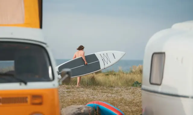 Mann mit SUP-Board am Strand von Fehmarn, bereit für die Wellen. Wohnmobile im Vordergrund.