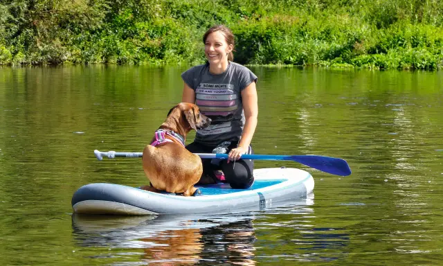 Frau und ihr sup hund krallen auf dem Fluss.