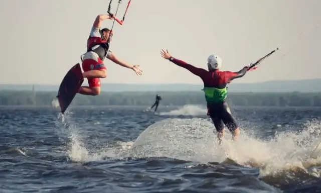 Zwei Kitesurfer springen und reichen sich die Hände auf dem Steinhuder Meer. Ein weiterer Surfer im Hintergrund.