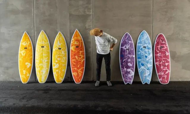 Mann mit Hut steht vor bunten Surfbrettern, bereit für das Wellenreiten.