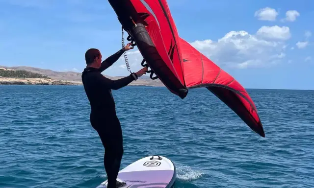Mann mit rotem Wingboard auf dem Wasser vor Costa Calma. Perfekter Tag für Wassersport am Ion Club.