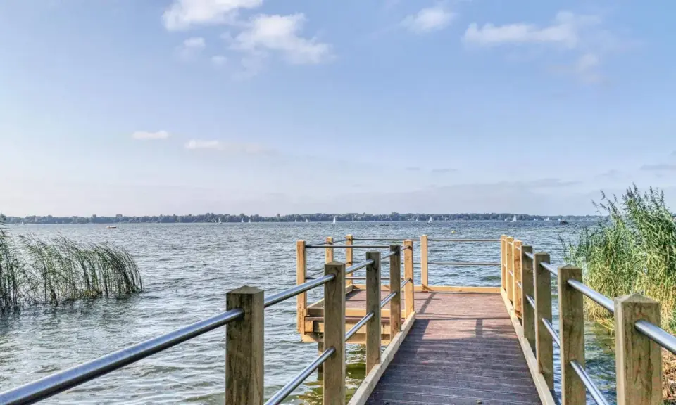 Holzsteg am Zwischenahner Meer mit Segelbooten am Horizont und Schilf am Ufer.