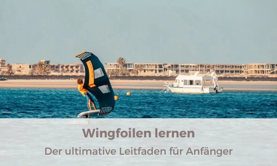 Person lernt wingfoilen auf dem Meer, mit einem Boot und Gebäuden im Hintergrund. Der ultimative Leitfaden für Anfänger.