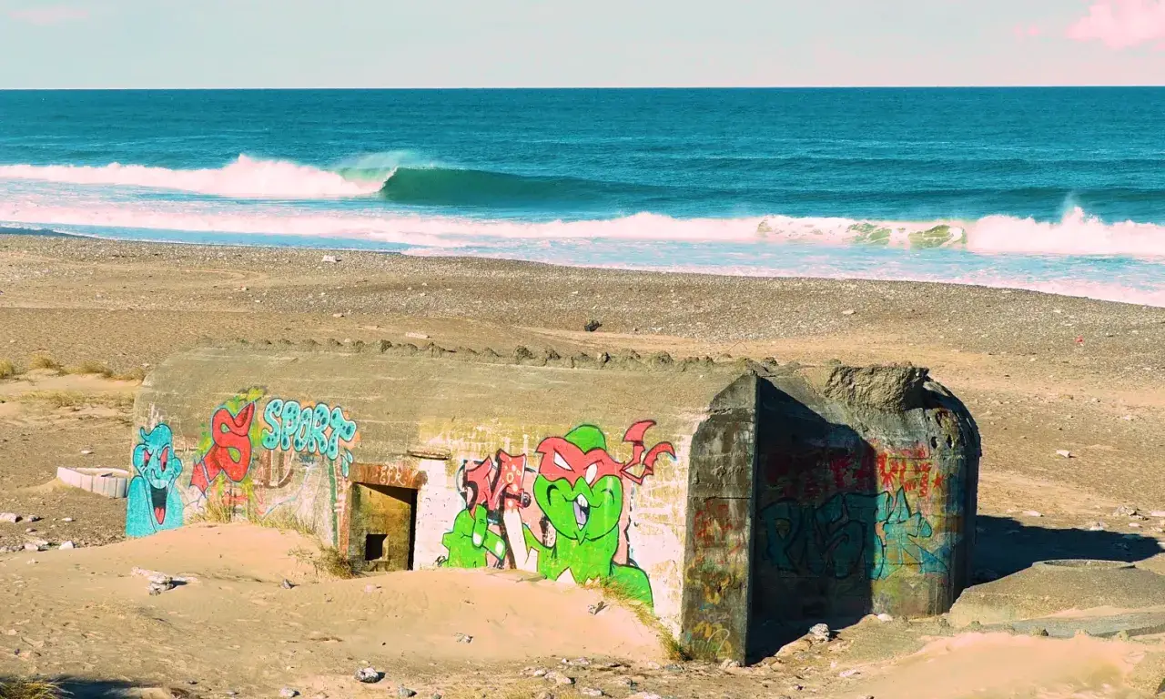 Bunker am Strand mit Graffiti, Wellen im Meer. Ein surreales, **cold hawaii**-Erlebnis.