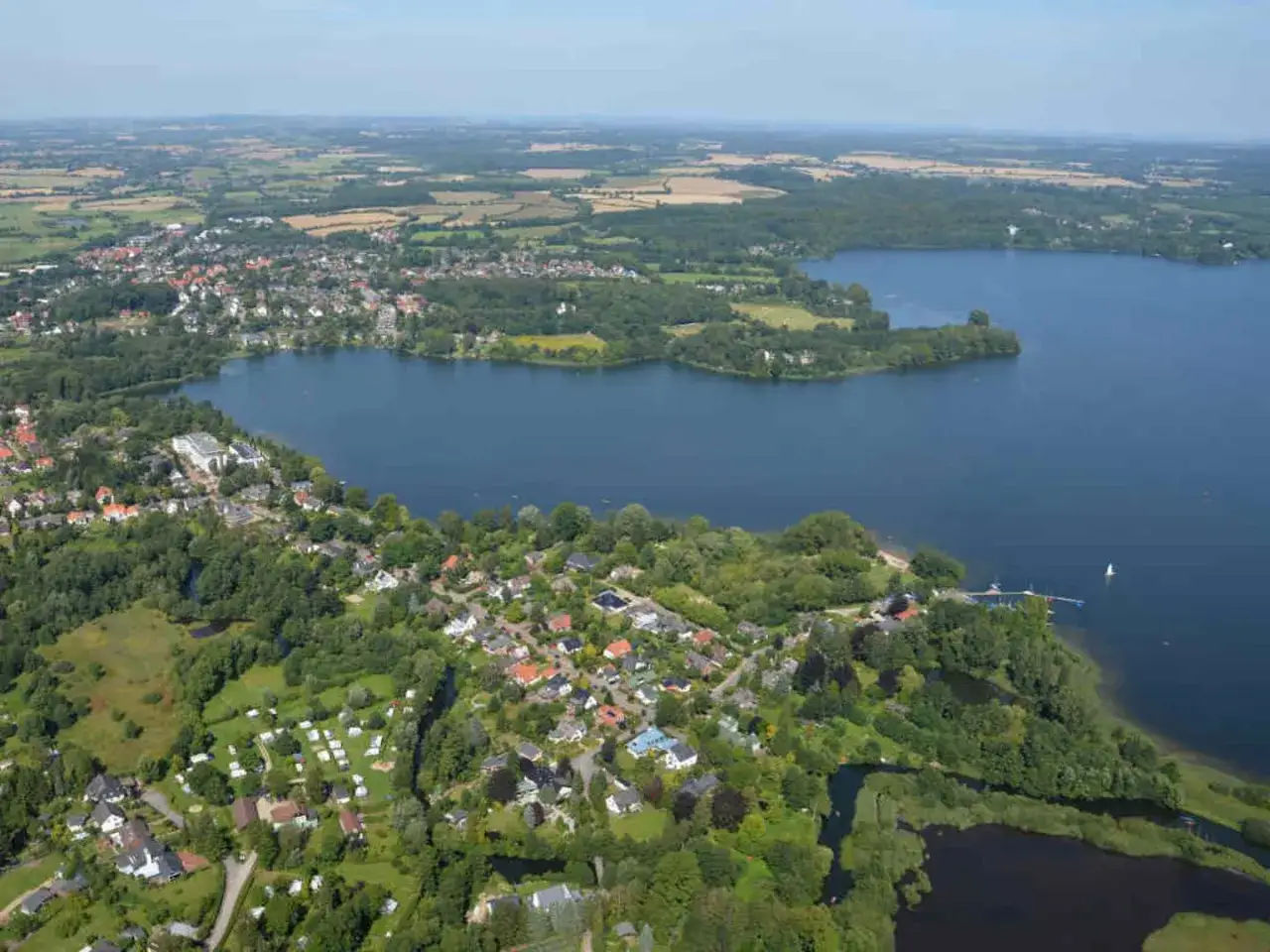 Luftaufnahme eines Sees mit umliegenden Häusern und Campingplatz in Schleswig-Holstein.