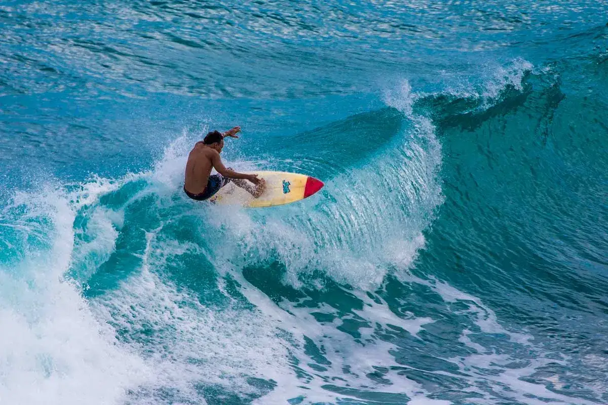 Ein Surfer reitet eine Welle an der Dominikanischen Republik. Das türkisfarbene Wasser bricht sich um ihn herum, während er auf seinem Brett balanciert.
