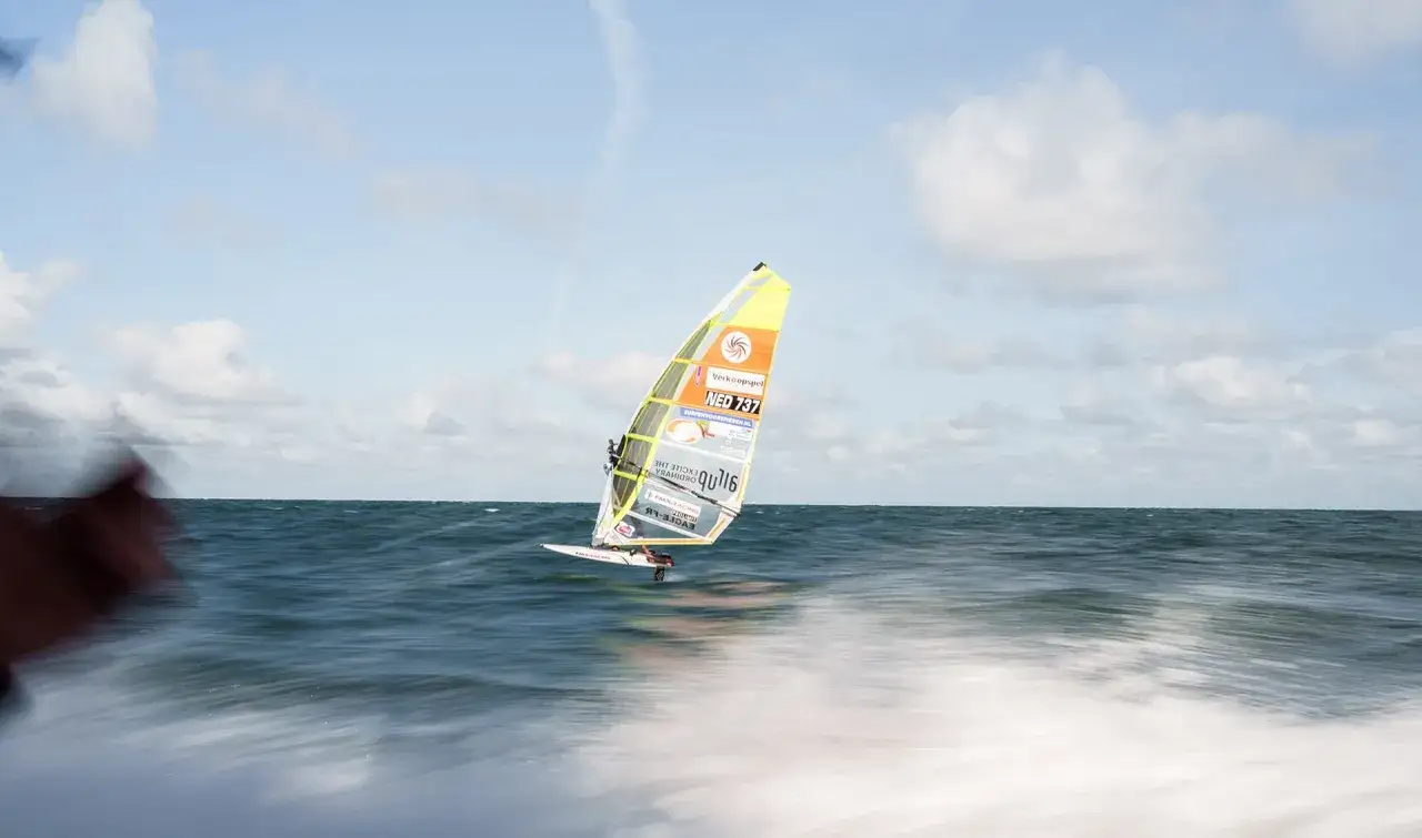 Ein Windsurfer gleitet über das Meer. Das bunte Segel mit der Aufschrift