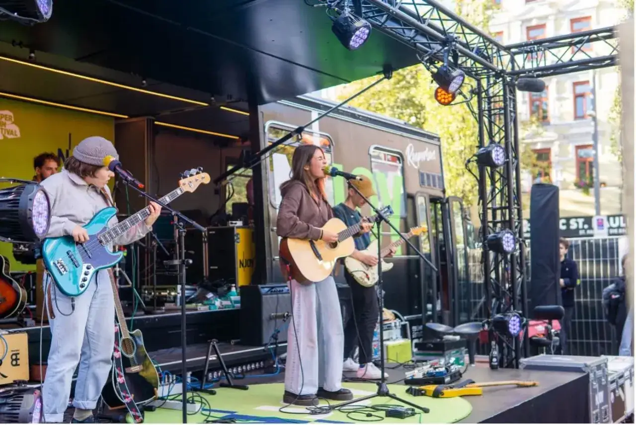 Band spielt auf einer Bühne beim sup fest. Eine Sängerin mit Gitarre, ein Bassist und ein Gitarrist geben alles.