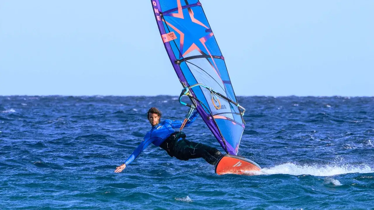 Windsurfer in Aktion vor Costa Calma, Fuerteventura. Der Mann im blauen Neoprenanzug gleitet &uuml;ber das Meer, die bunte Segel &uuml;ber ihm.