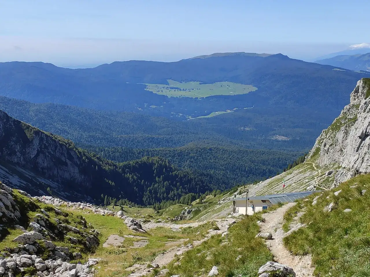 Bergpanorama mit Hütte und einem grünen Tal, das an den Lago di Santa Croce erinnert.