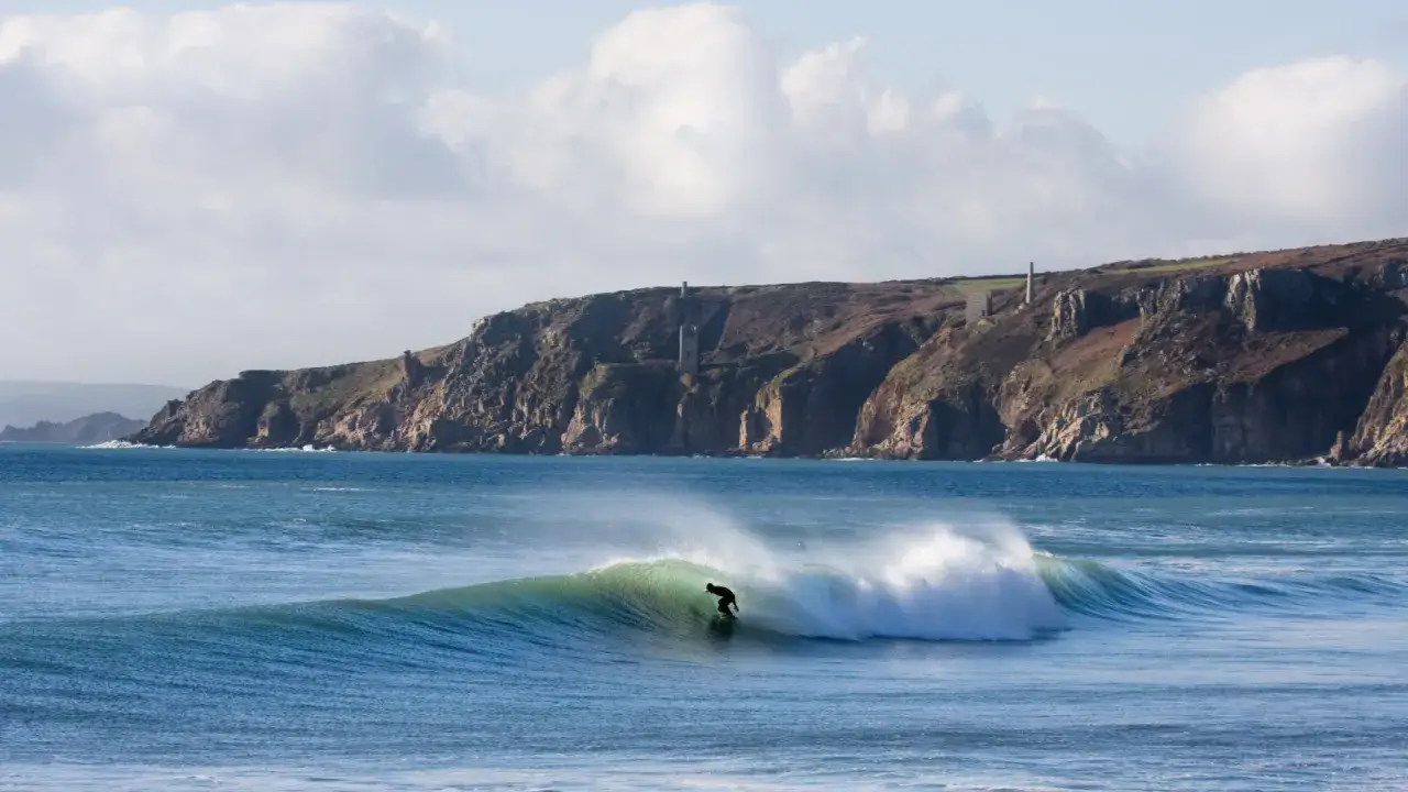 Ein Surfer reitet eine grüne Welle vor der dramatischen Küste Cornwalls.