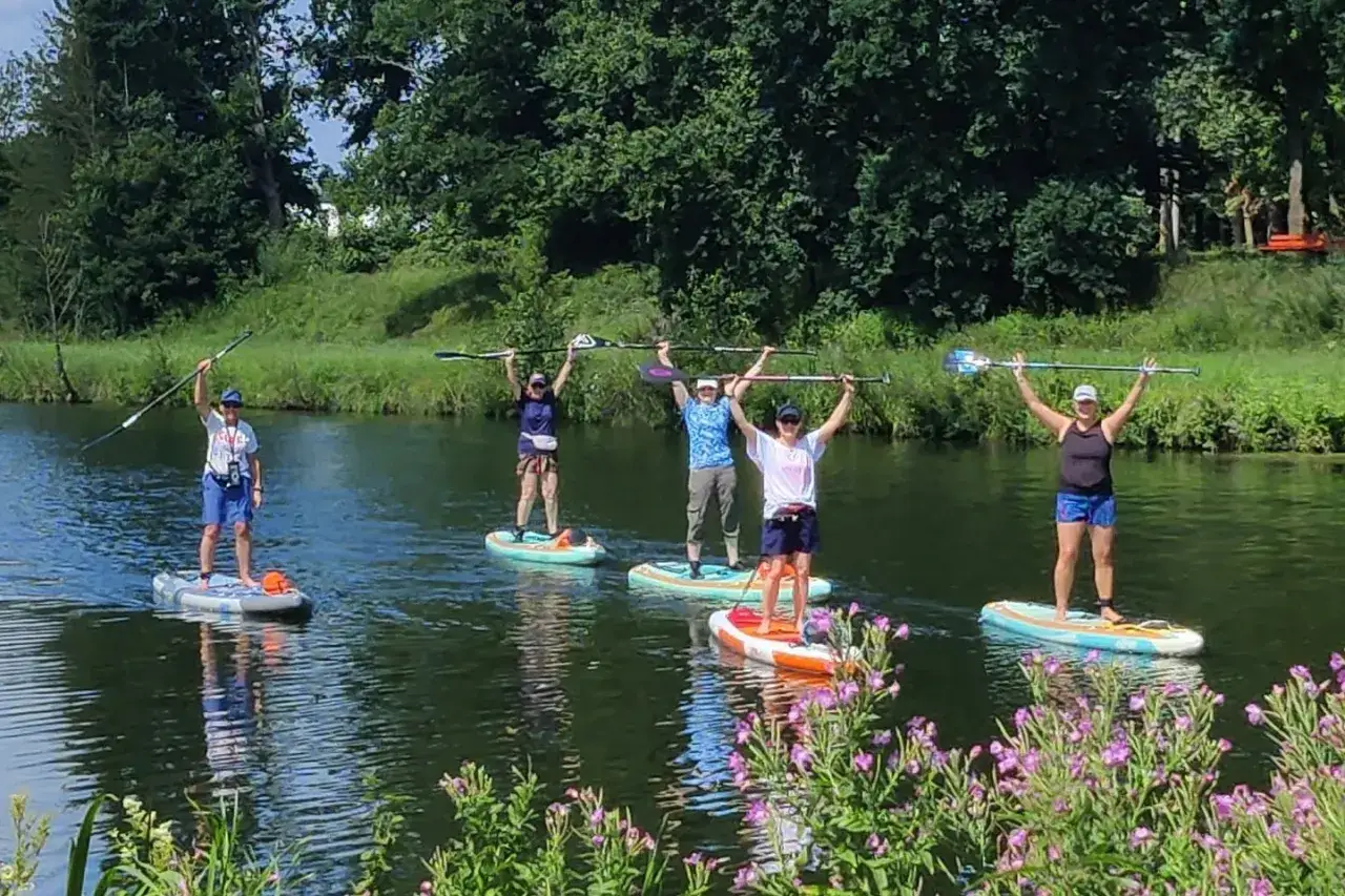 Fünf Personen genießen SUP NRW auf einem ruhigen Fluss, die Paddel hoch in die Luft gestreckt.