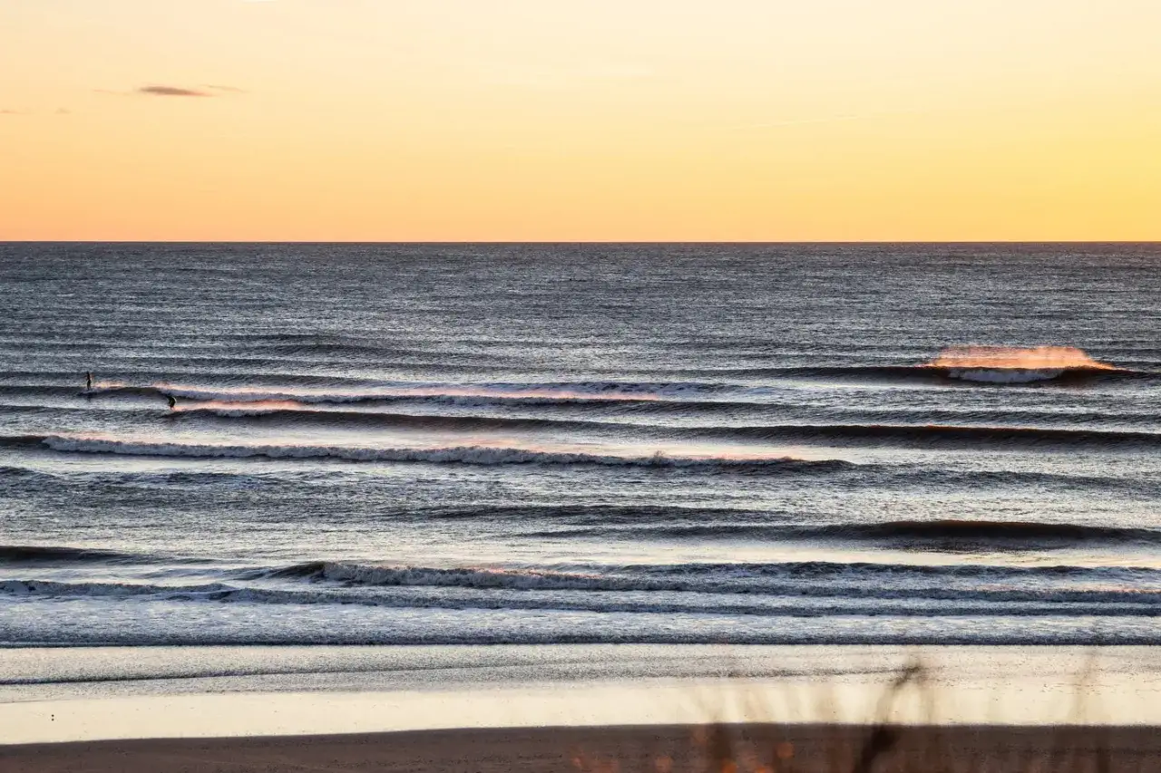Zwei Surfer genießen die Wellen bei Hvide Sande. Die Sonne taucht den Himmel in warmes Orange.