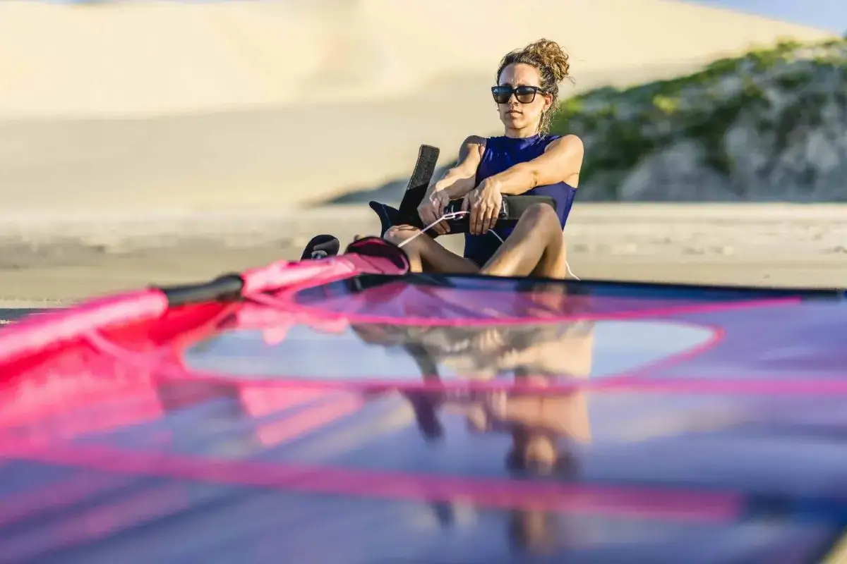 Frau mit Sonnenbrille bereitet sich auf das Windsurfen vor, pr&uuml;ft die Segelleinen. Viele Windsurfen Begriffe sind hier relevant.