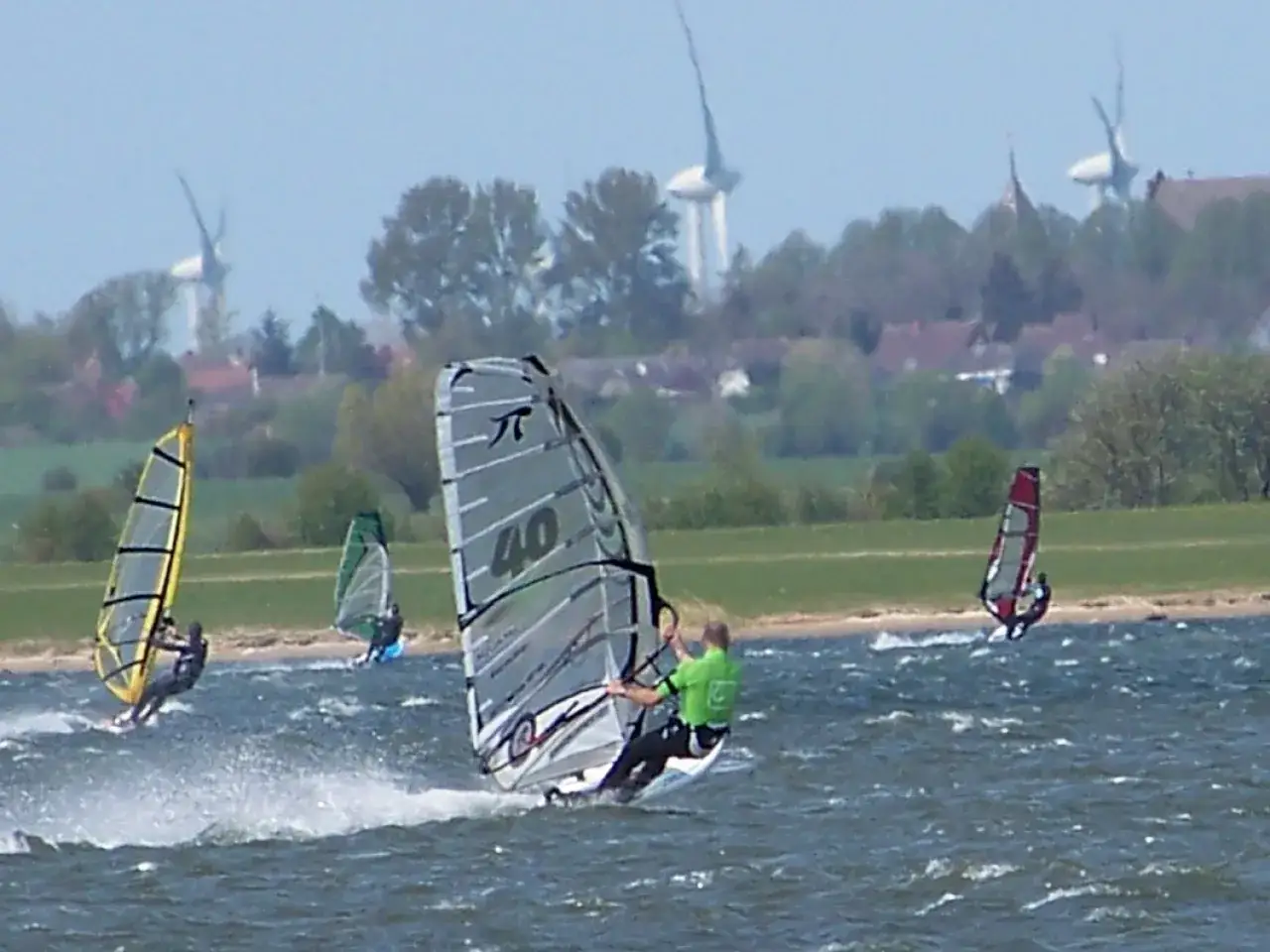 Windsurfer auf dem Wasser bei Wulfen, mit Windrädern im Hintergrund.