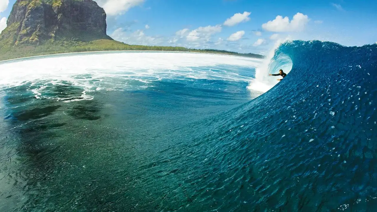 Surfer reitet eine perfekte Welle vor der Küste von Mauritius, mit dem ikonischen Berg Le Morne im Hintergrund.