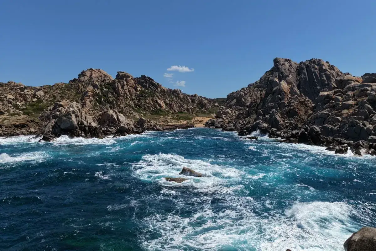 Tosende Wellen brechen an den Felsen des Capo Testa auf Sardinien. Ein dramatischer Küstenabschnitt mit zerklüfteten Granitformationen und tiefblauem Meer.