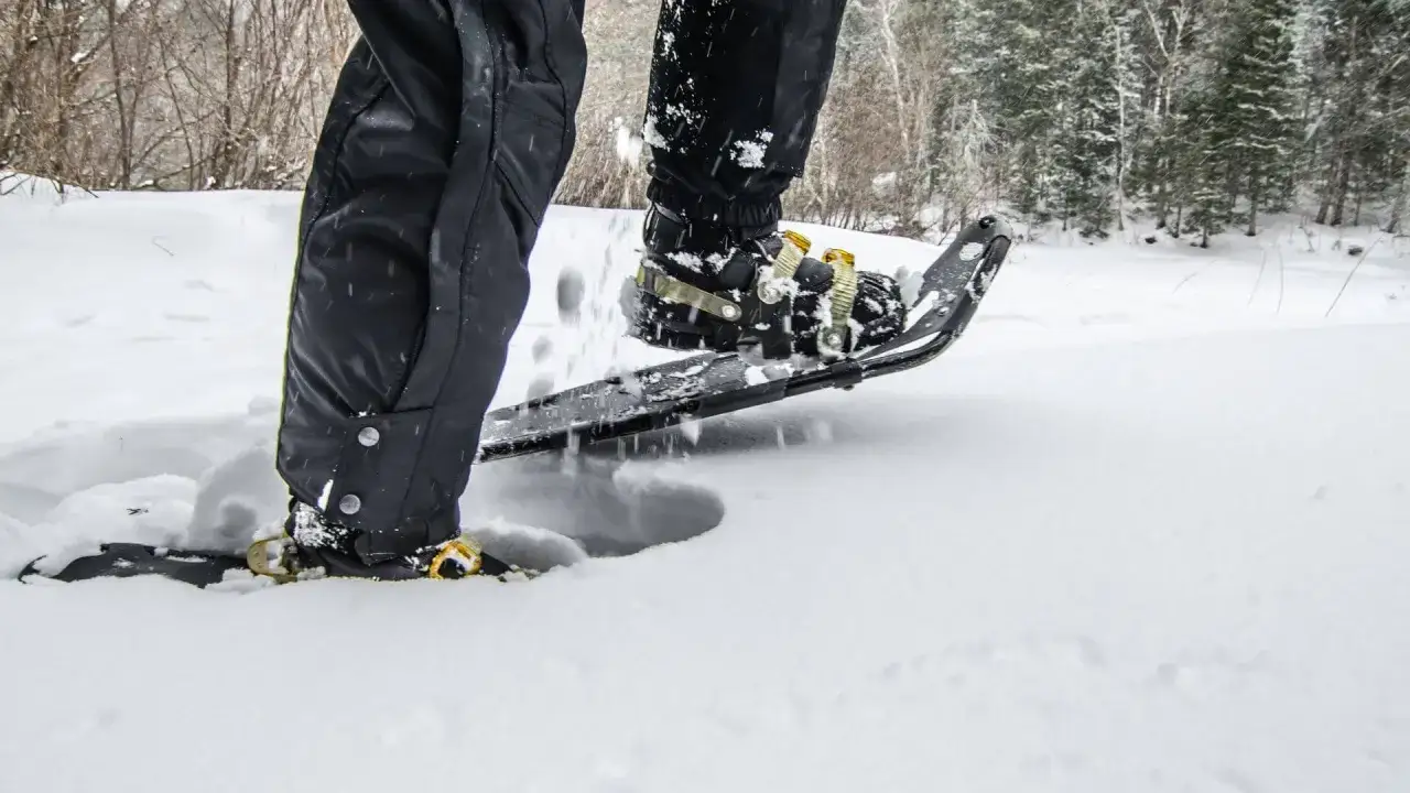 Schneeschuhwandern Schuhe sinken tief in den Schnee. Ein Mann in schwarzer Hose stapft durch die Winterlandschaft.