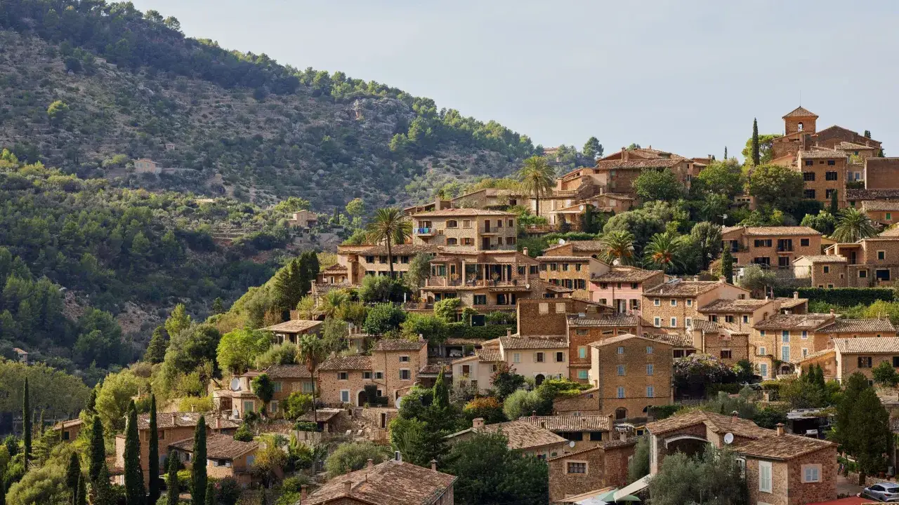 Ein malerisches Dorf mit Steinhäusern schmiegt sich an einen grünen Hang auf Mallorca.