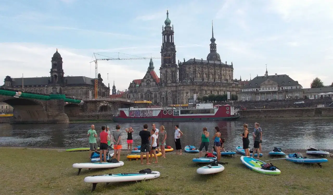 SUP-Fans am Elbufer in Dresden, bereit f&uuml;r eine Tour mit der Frauenkirche im Hintergrund.