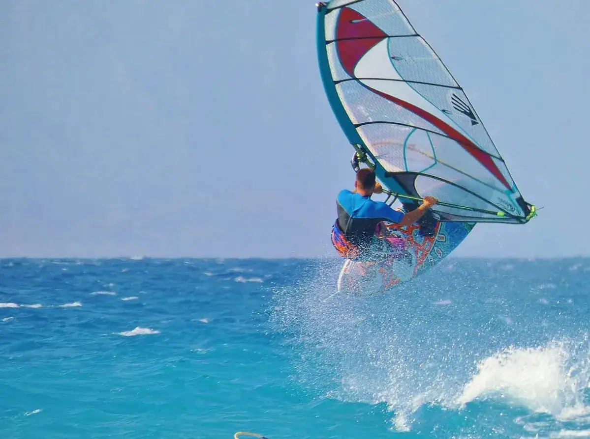 Ein Windsurfer springt hoch über dem türkisfarbenen Meer. Ein typischer Anblick beim Windsurfen Griechenland.