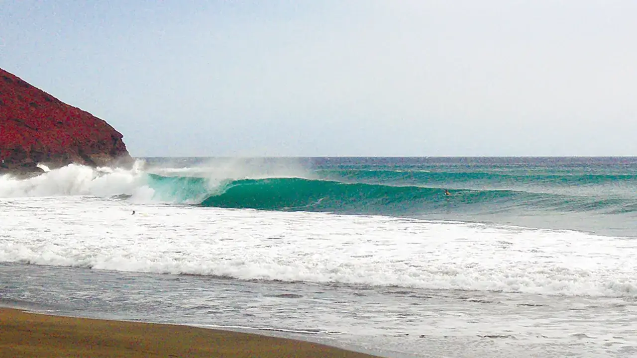 Grüne Wellen brechen an der Küste von La Gomera. Ein Surfer wartet auf die perfekte Welle.