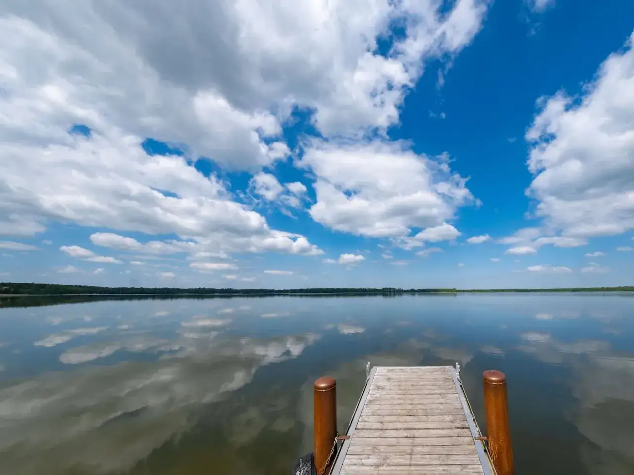 Holzsteg an einem See mit spiegelglatter Wasseroberfläche, die den dramatischen Wolkenhimmel reflektiert. Ein friedlicher Anblick, seen in Sachsen-Anhalt.