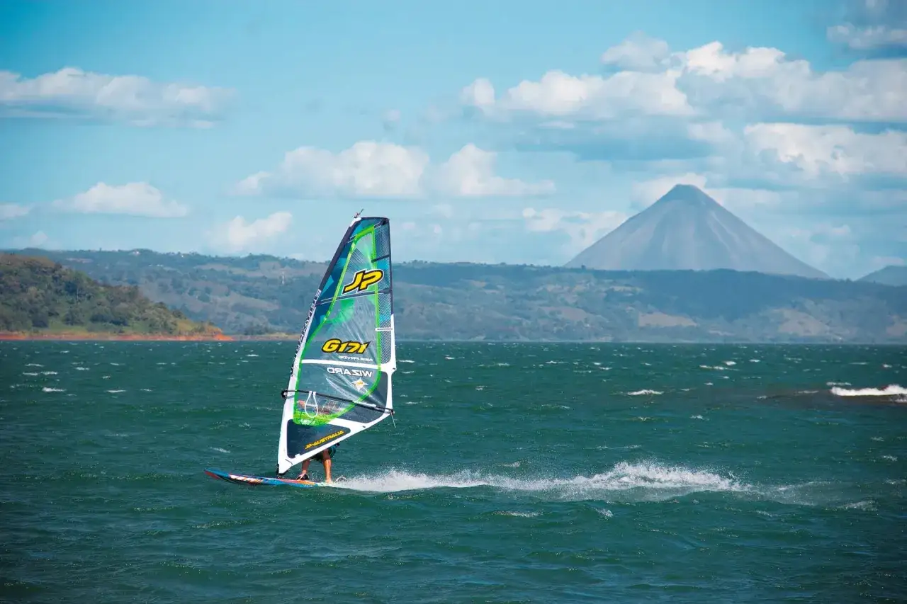 Windsurfer gleitet &uuml;ber den Arenal See, im Hintergrund der majest&auml;tische Vulkan.