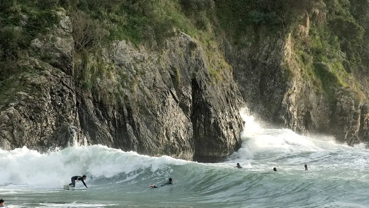 Surfer reitet eine Welle vor steiler Felswand. Mehrere Surfer im Wasser, die die Wellen genießen. Rhodos Surfen ist ein aufregendes Erlebnis.