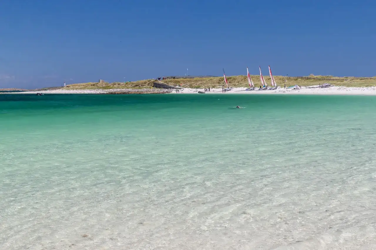 T&uuml;rkisblaues Wasser und wei&szlig;e Sandstr&auml;nde auf den Glenan Inseln. Kleine Segelboote und ein Schwimmer genie&szlig;en die Sonne.