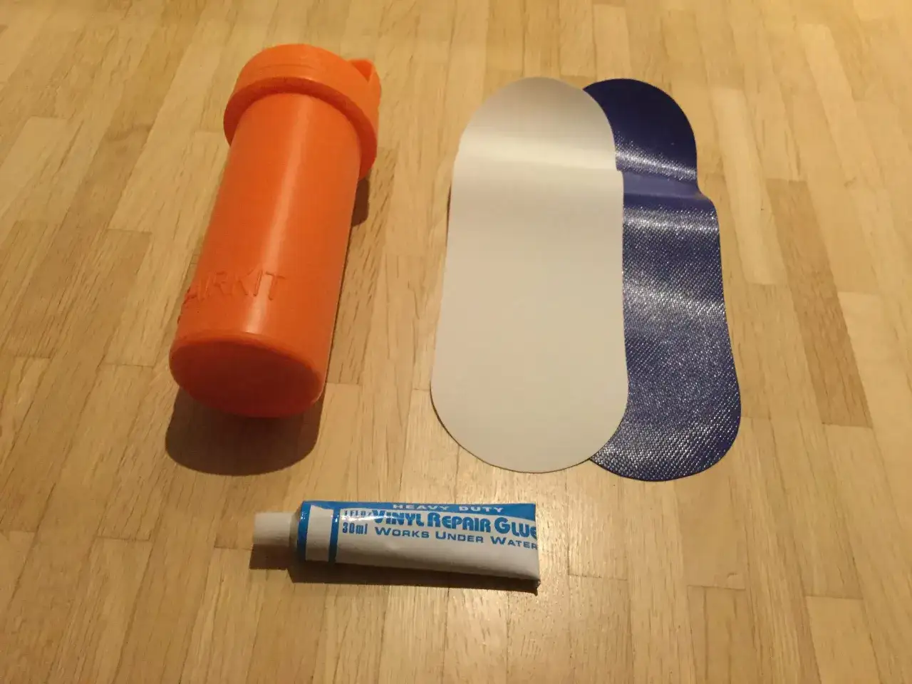 Reparaturset für Schlauchboote: orange Dose, weiße und blaue Flicken, sowie ein sup kleber für Vinyl.