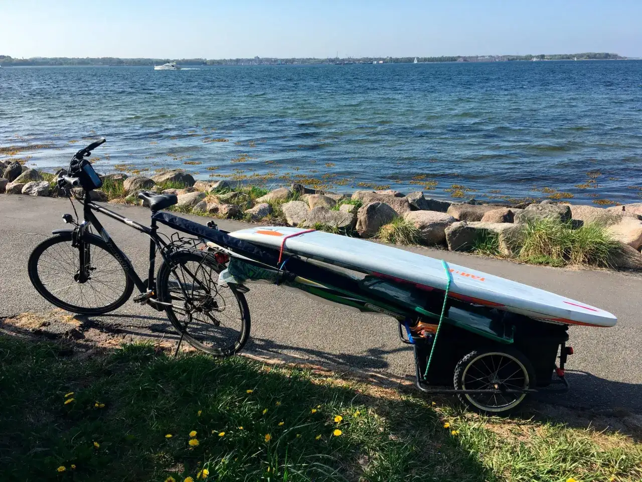 Fahrradanhänger mit Surfbrett beladen, bereit für eine Tour am Wasser.